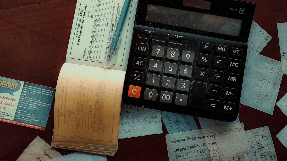 Calculadora preta sobre mesa de madeira cercada por recibos e papéis de contas