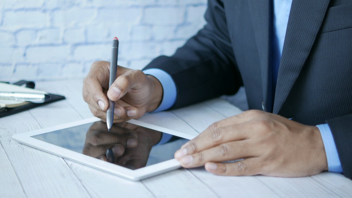 Homem de terno escrevendo com caneta digital na tela de um tablet sobre a mesa