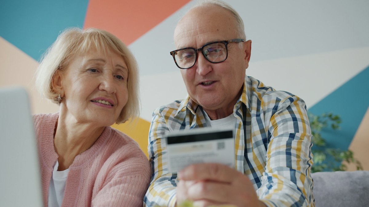 Casal de idosos sentado lado a lado observando um cartão bancário nas mãos do homem