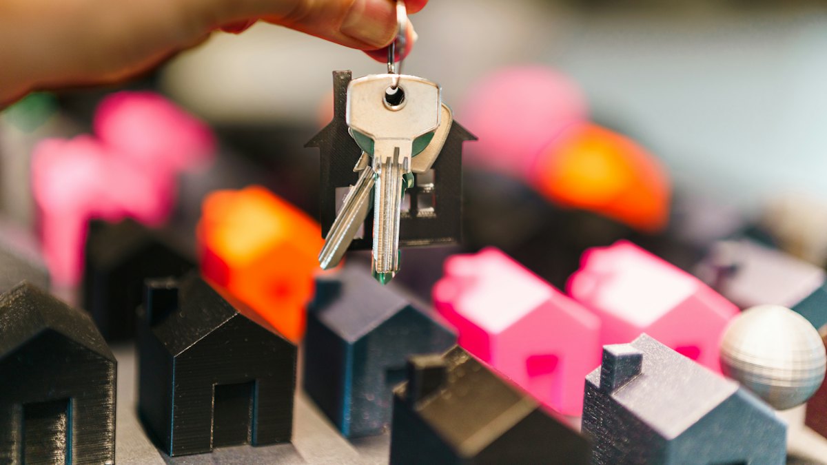Mão segurando chaves de casa sobre miniaturas de casas coloridas