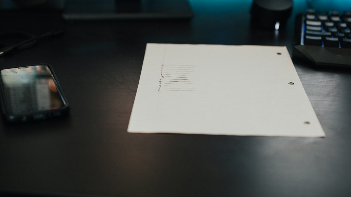 Folha de papel em branco sobre mesa escura com teclado e luz azul ao fundo