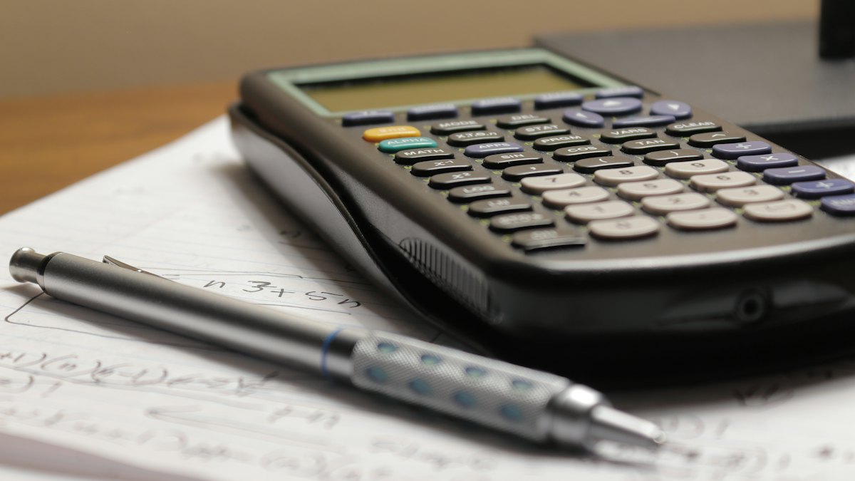 Calculadora preta e lapiseira sobre folhas de papel com anotações em uma mesa