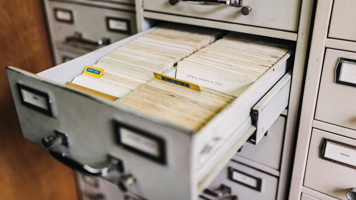 Gaveta de arquivo de metal aberta com fichas e pastas organizadas em fileiras