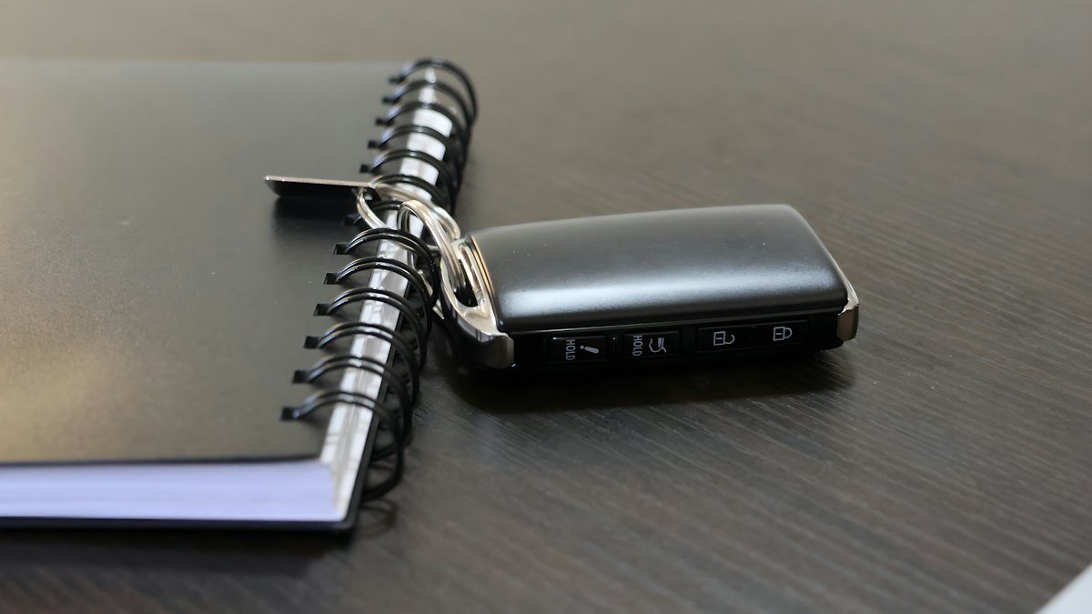 Chave de carro preta apoiada sobre um caderno espiral em mesa escura